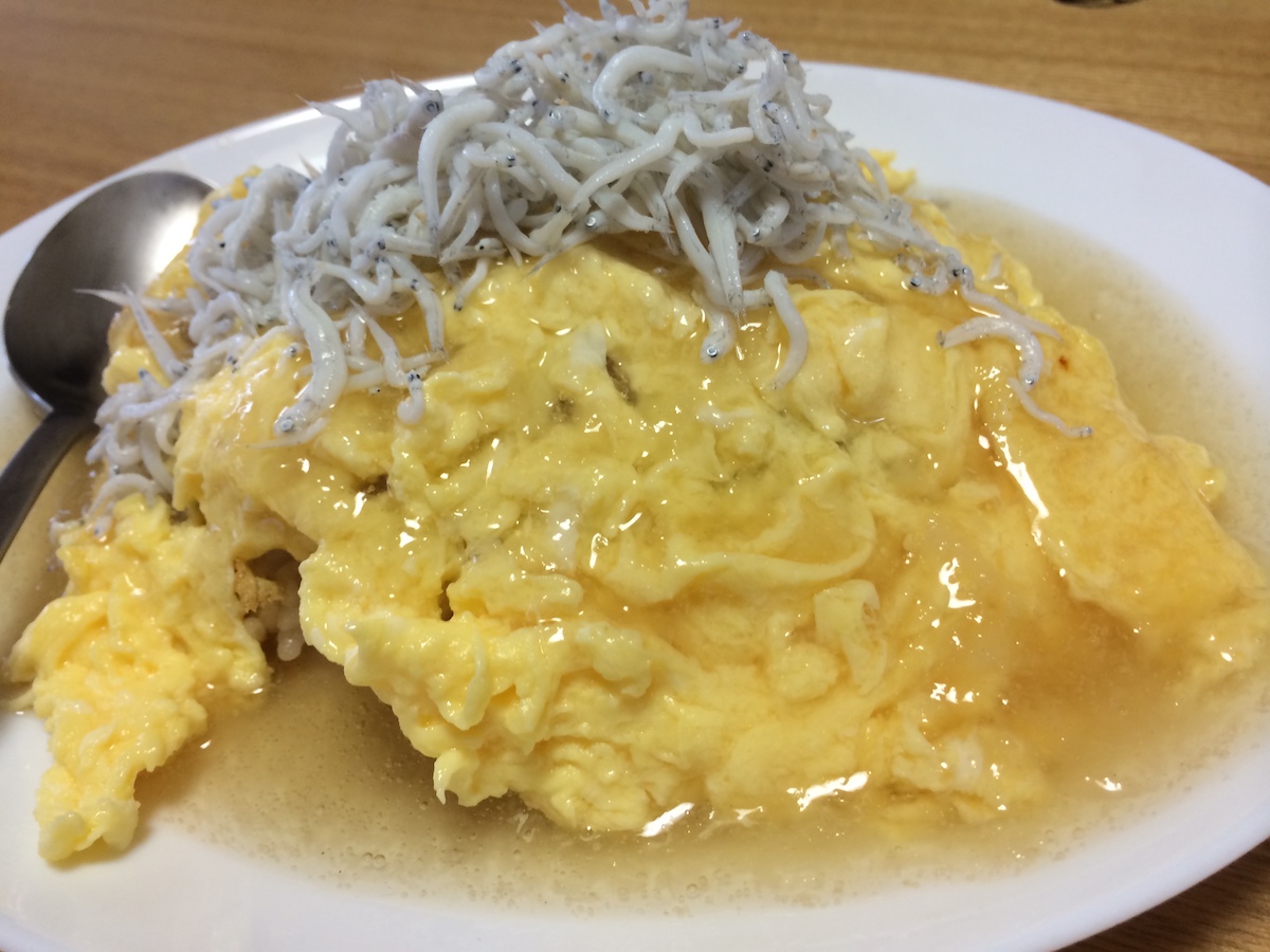 Softly fried egg on top of fried rice with starchy sauce. Whitebait is on top of them to taste.