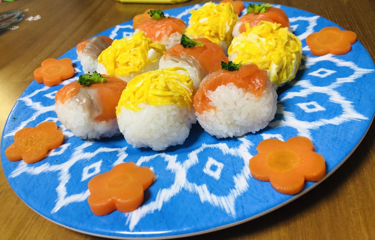 4 pieces of salmon sushi balls and 4 pieces of egg sushi balls on a blue plate.
