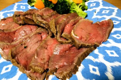10 pieces of sliced roast beef with cooked broccoli and carrots on a blue plate.