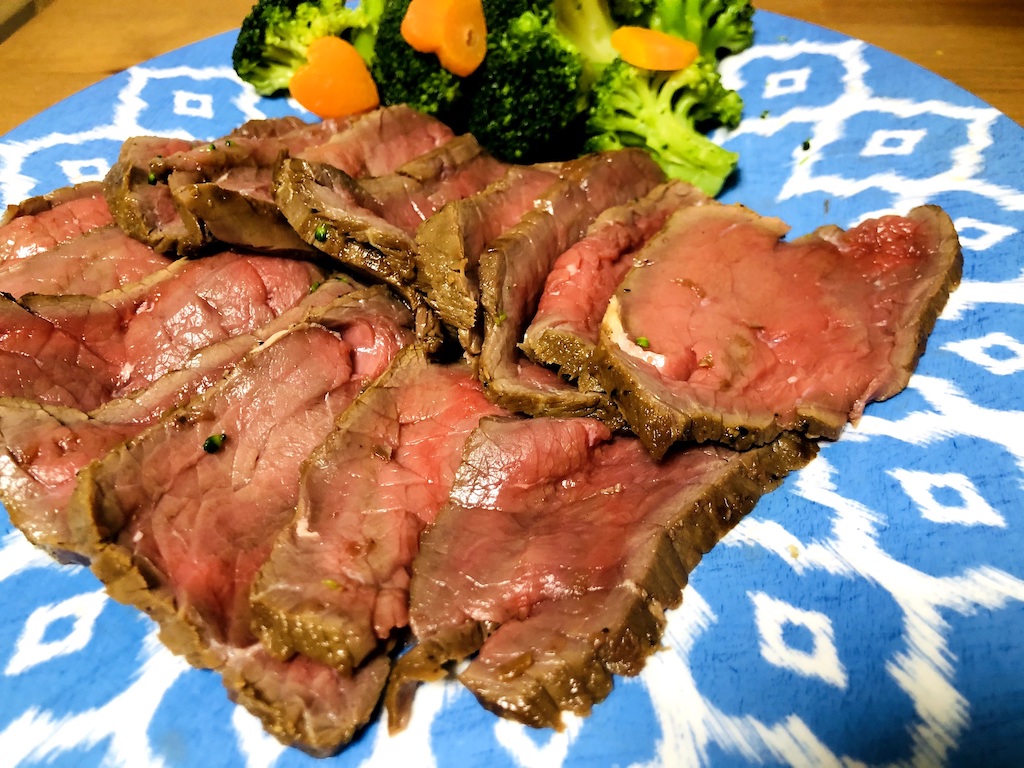 10 pieces of sliced roast beef with cooked broccoli and carrots on a blue plate.